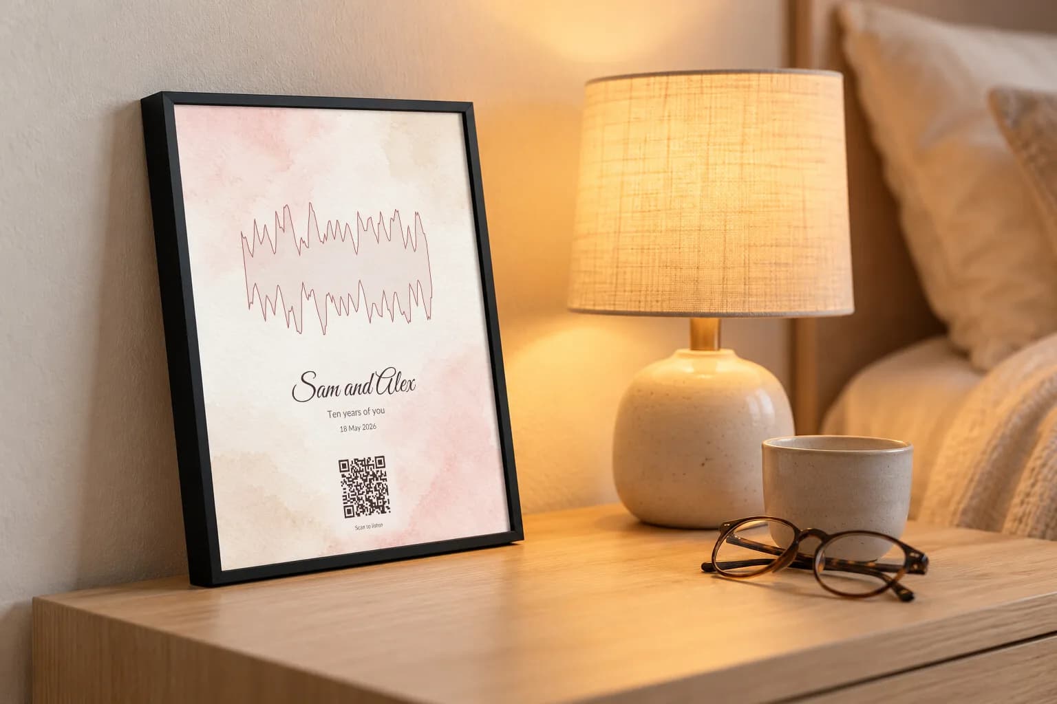 A watercolour voice print for Sam and Alex on a bedside table by a lamp
